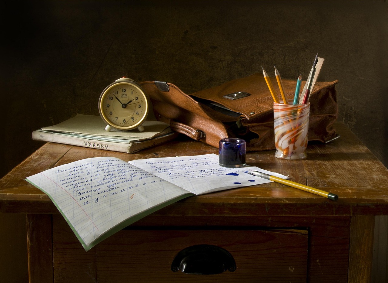 A vintage clock, notebook, and pencil holder on a wood desk