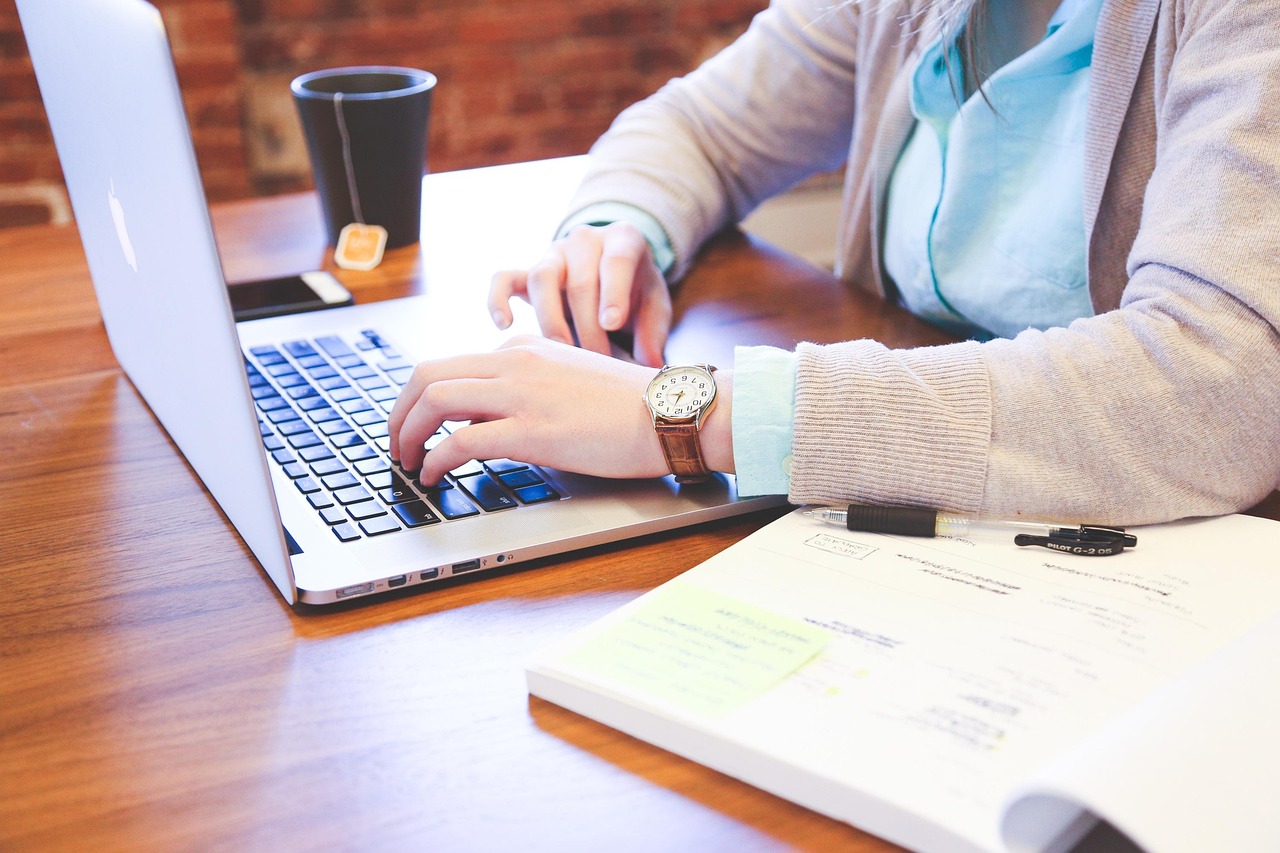 A person typing on a laptop at a wooden desk with coffee nearby