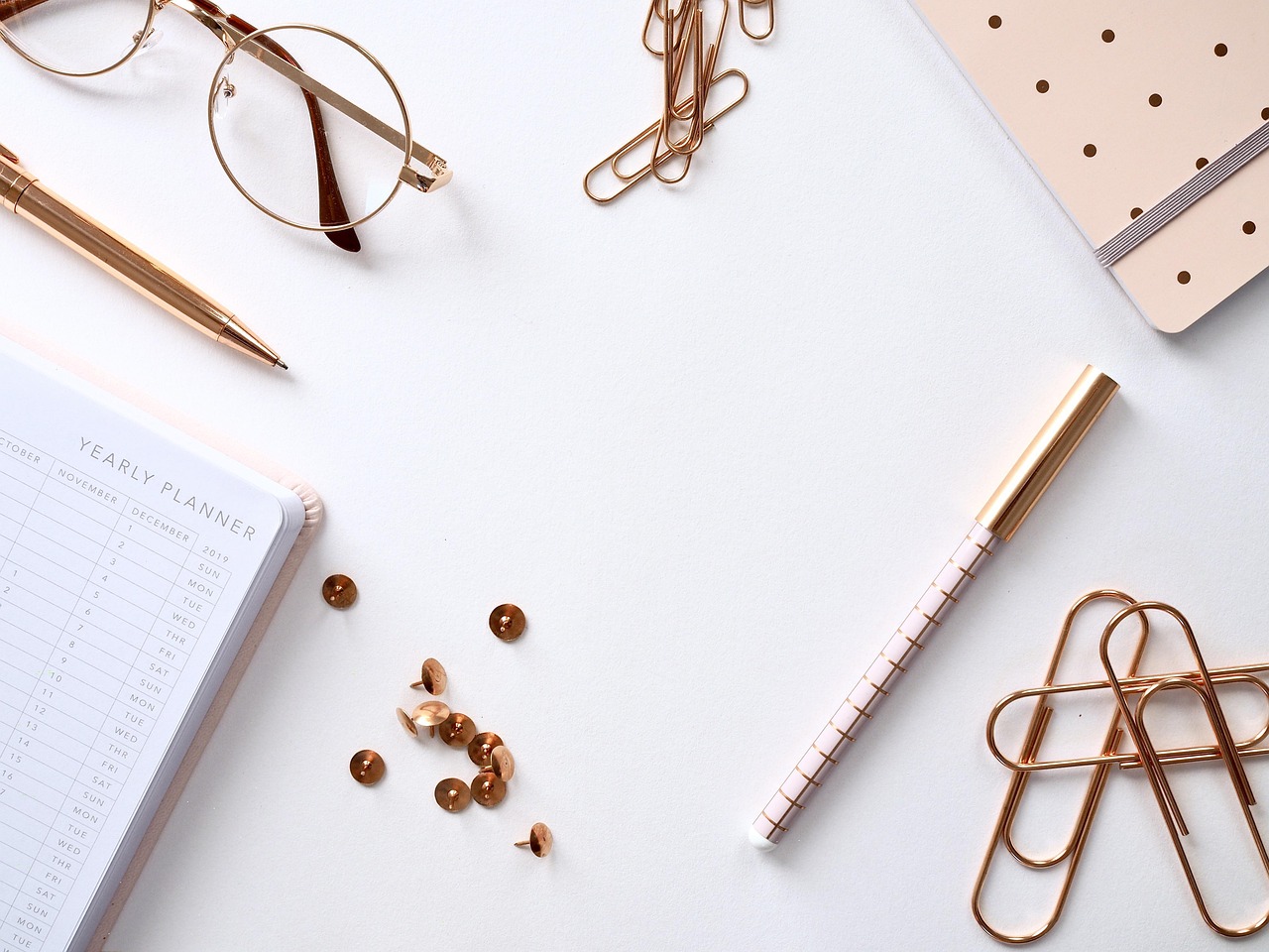 A notebook, glasses, and paperclips arranged on a cream desk